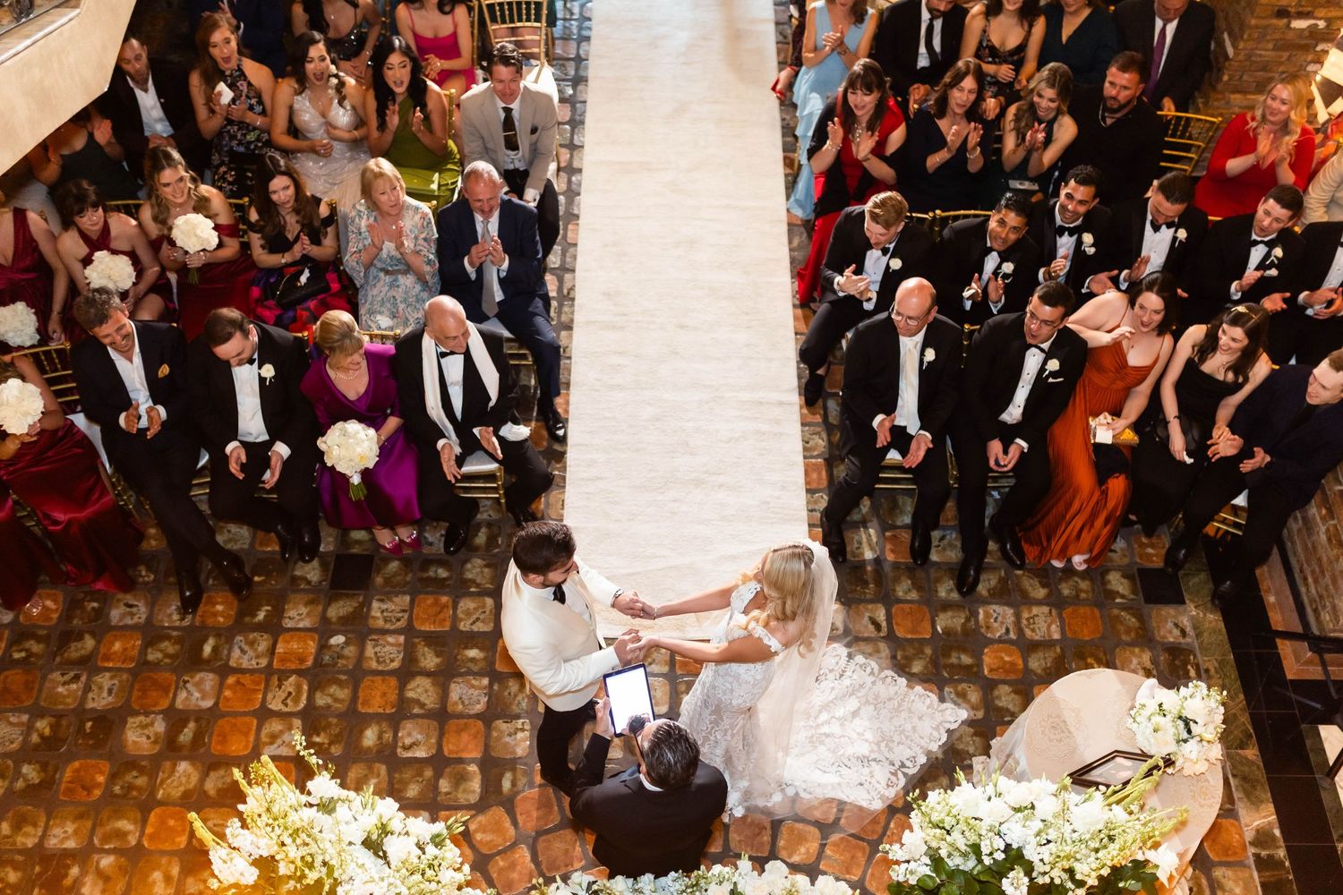 Overhead view of wedding ceremony in elegant indoor venue with brick walls and decorative lighting.
