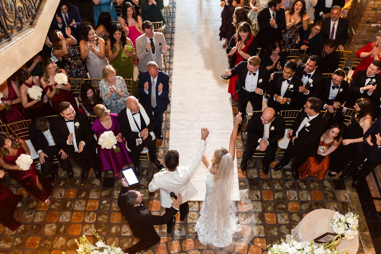 Panoramic view of wedding ceremony with guests seated in historic brick-walled venue.