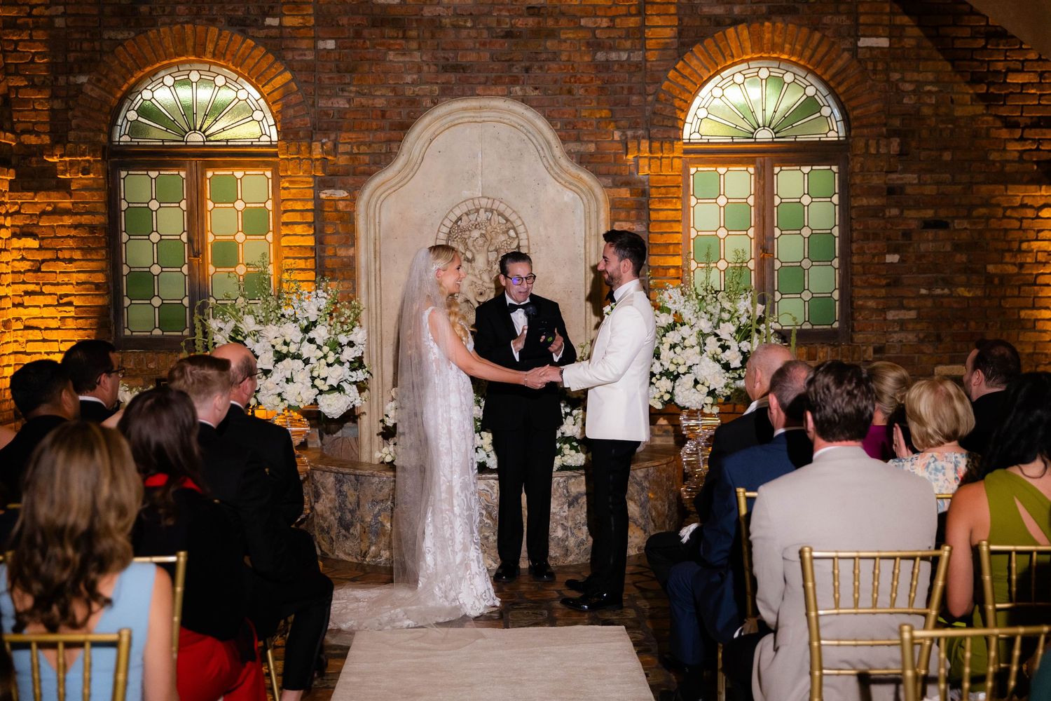 Wedding ceremony in a rustic brick venue with arched windows and floral arrangements.