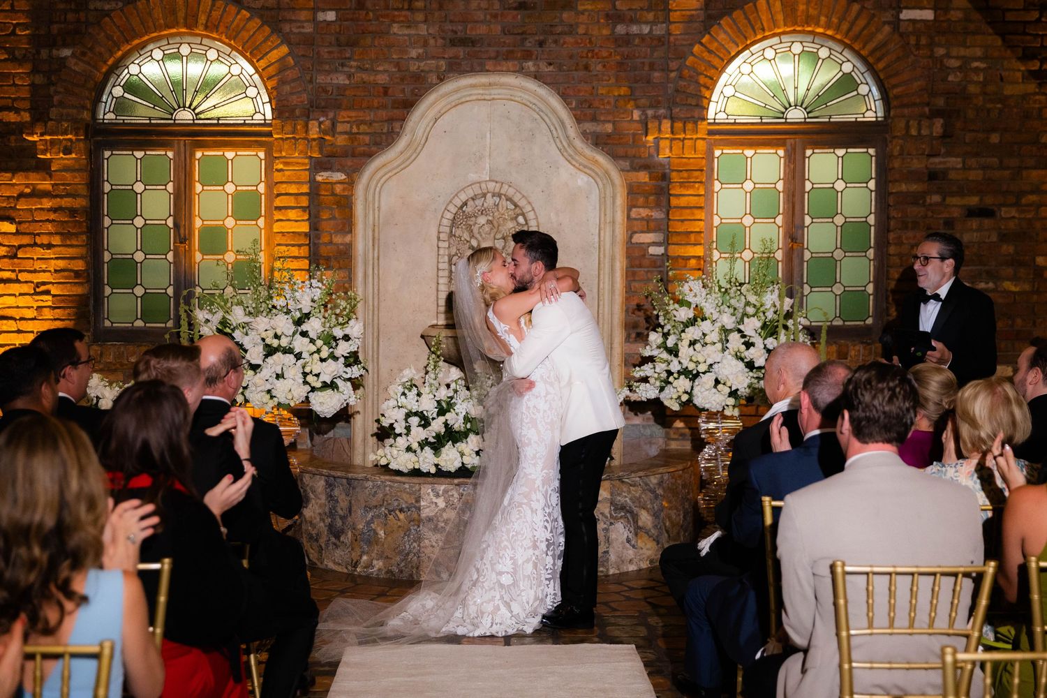 Wedding celebration scene in a historic brick venue with elegant decor and crowd of guests.