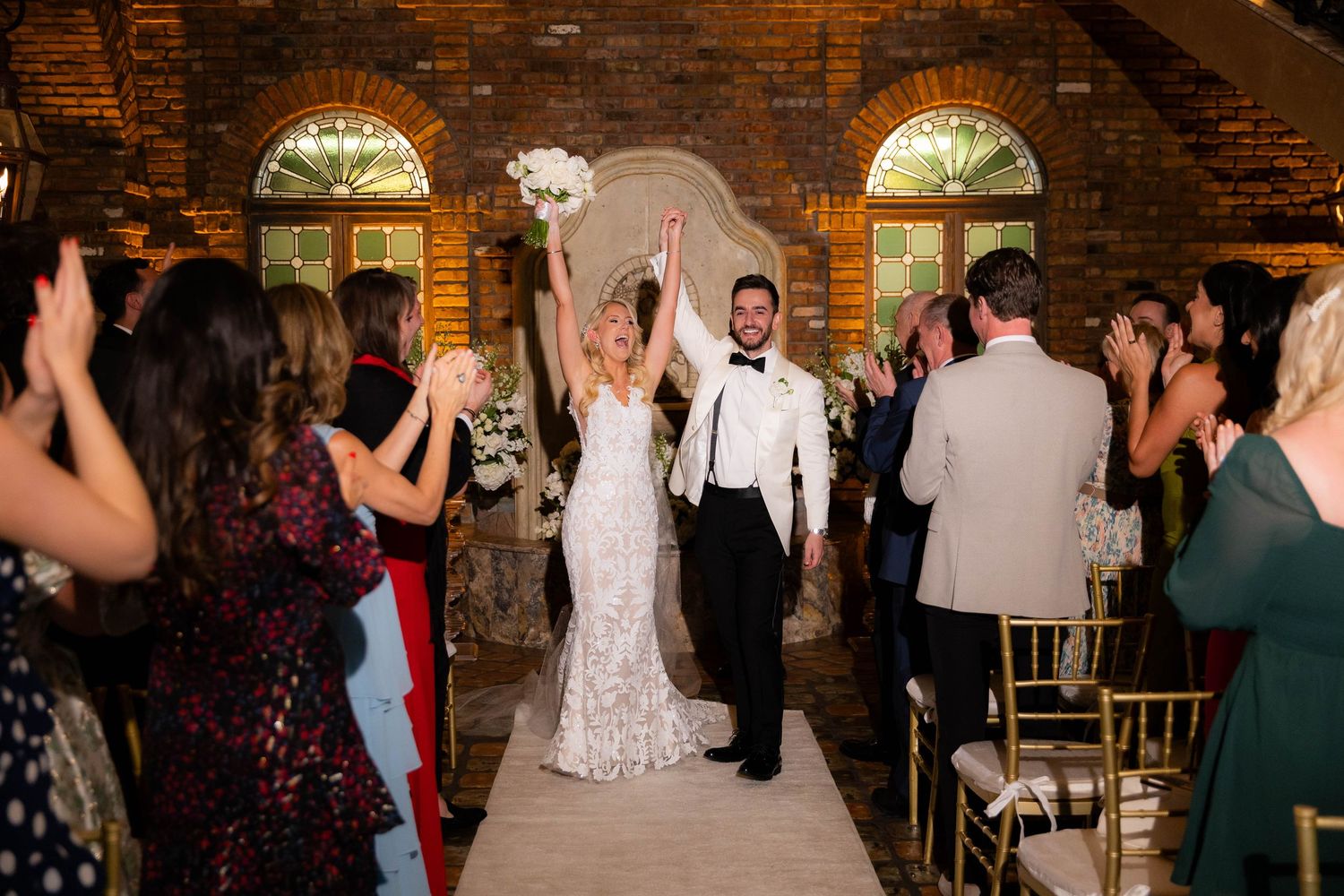 Wedding ceremony taking place in rustic venue with exposed brick walls and arched windows.