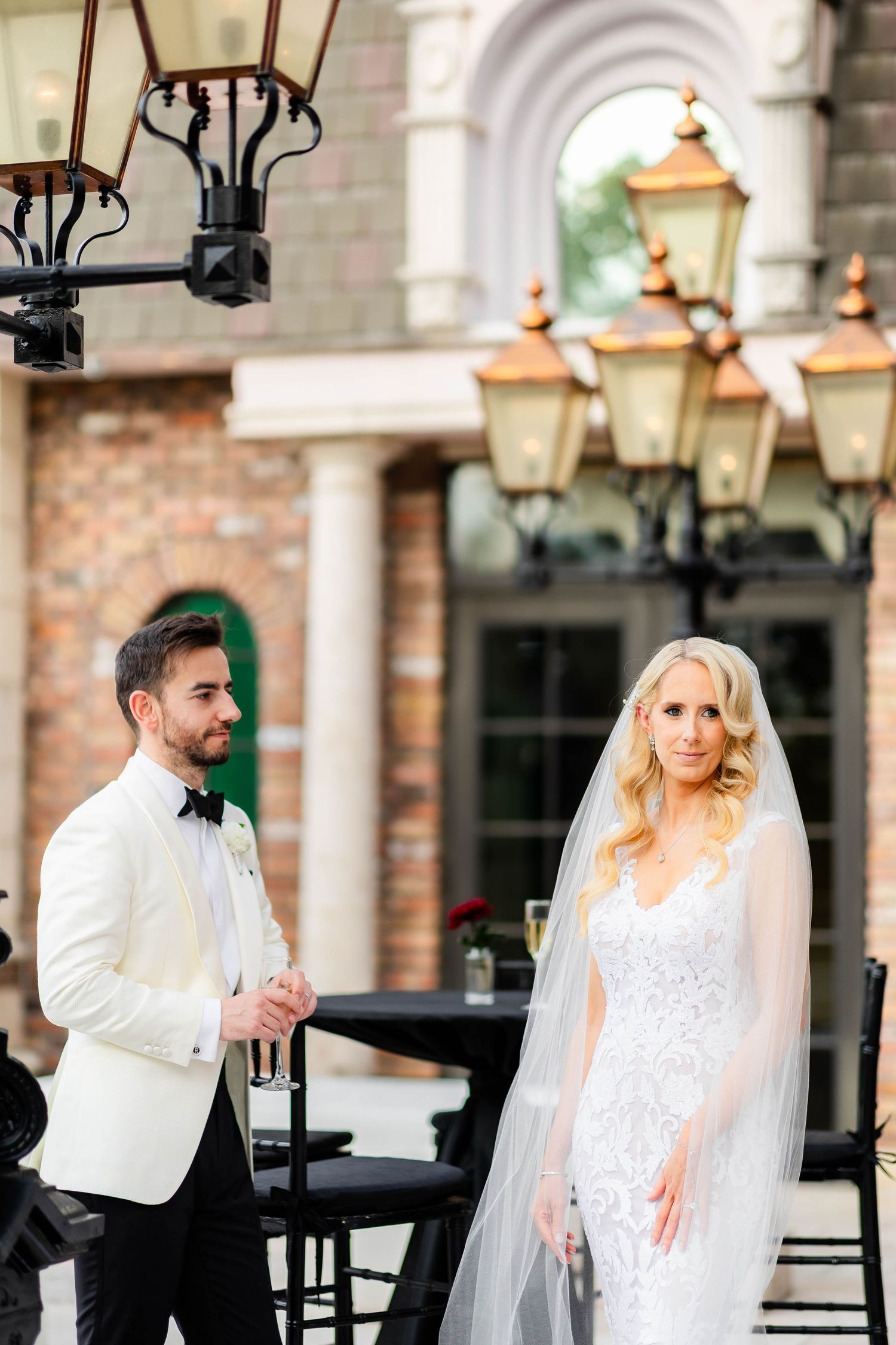 Couple poses for portraits under elegant outdoor lanterns and brick architecture.