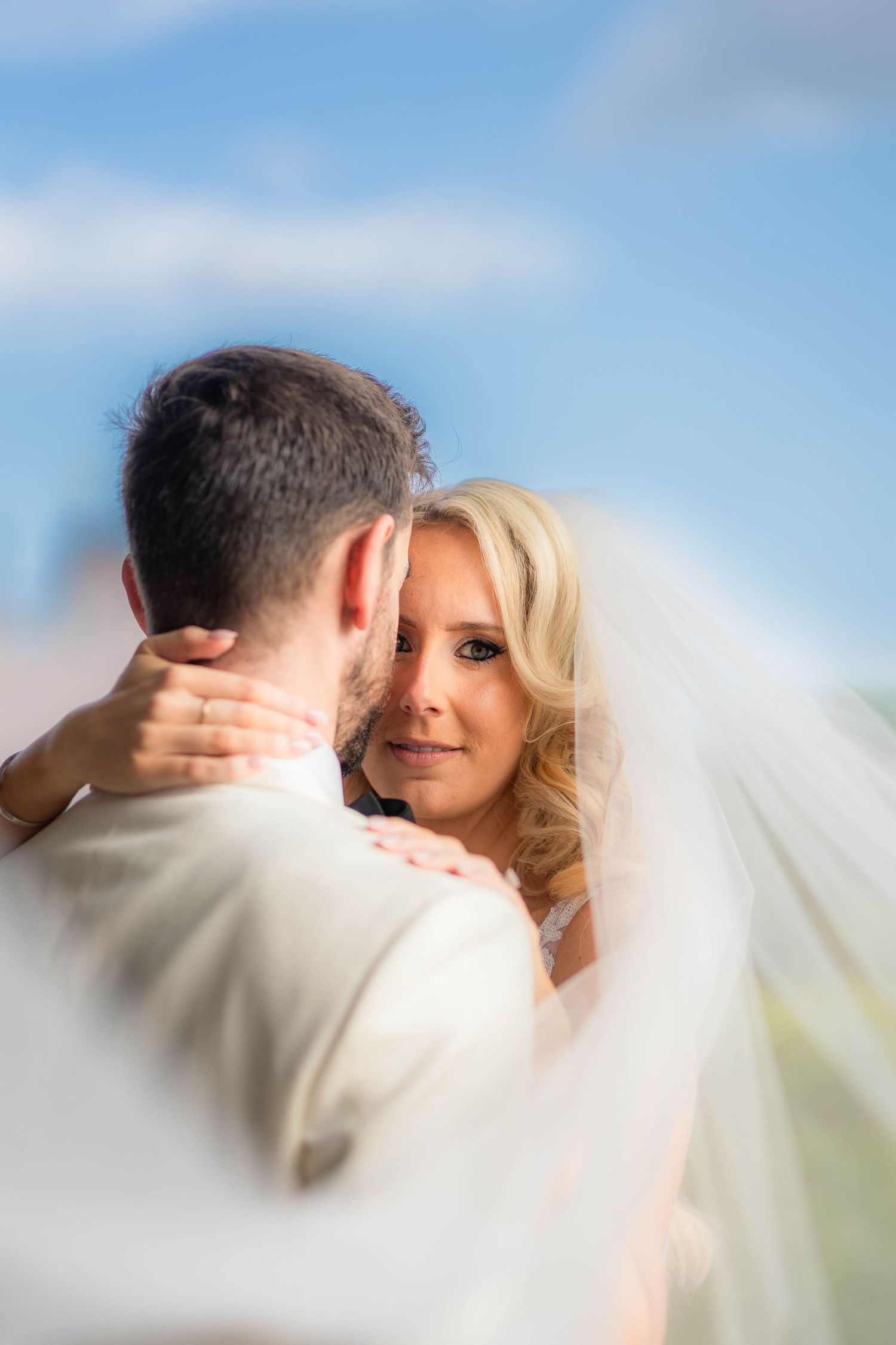 Close-up romantic moment between newlyweds against blue sky backdrop.