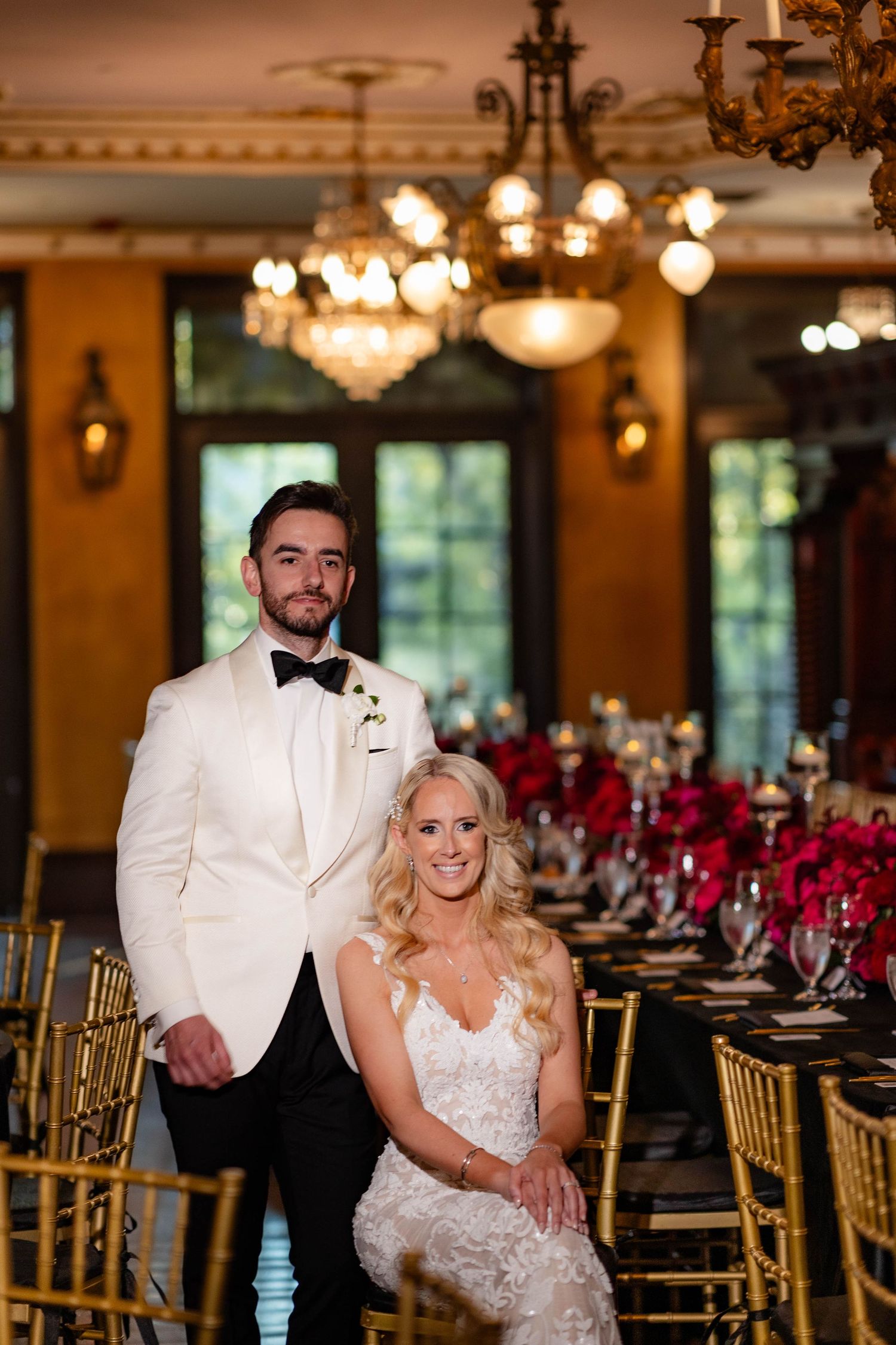 Reception venue features gold chiavari chairs, crystal chandeliers and romantic red floral arrangements.
