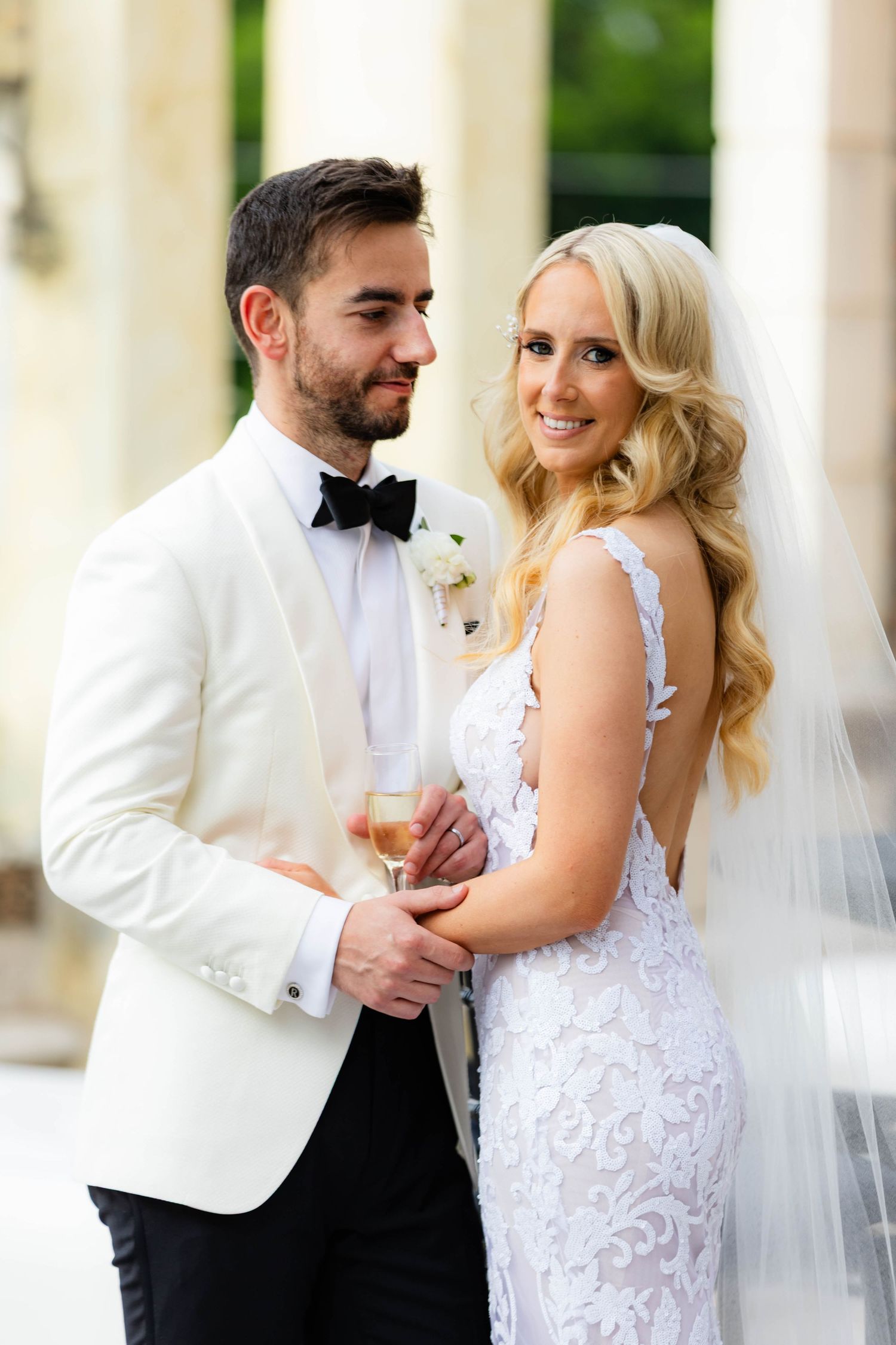 Elegant wedding portraits against white columns in formal attire.