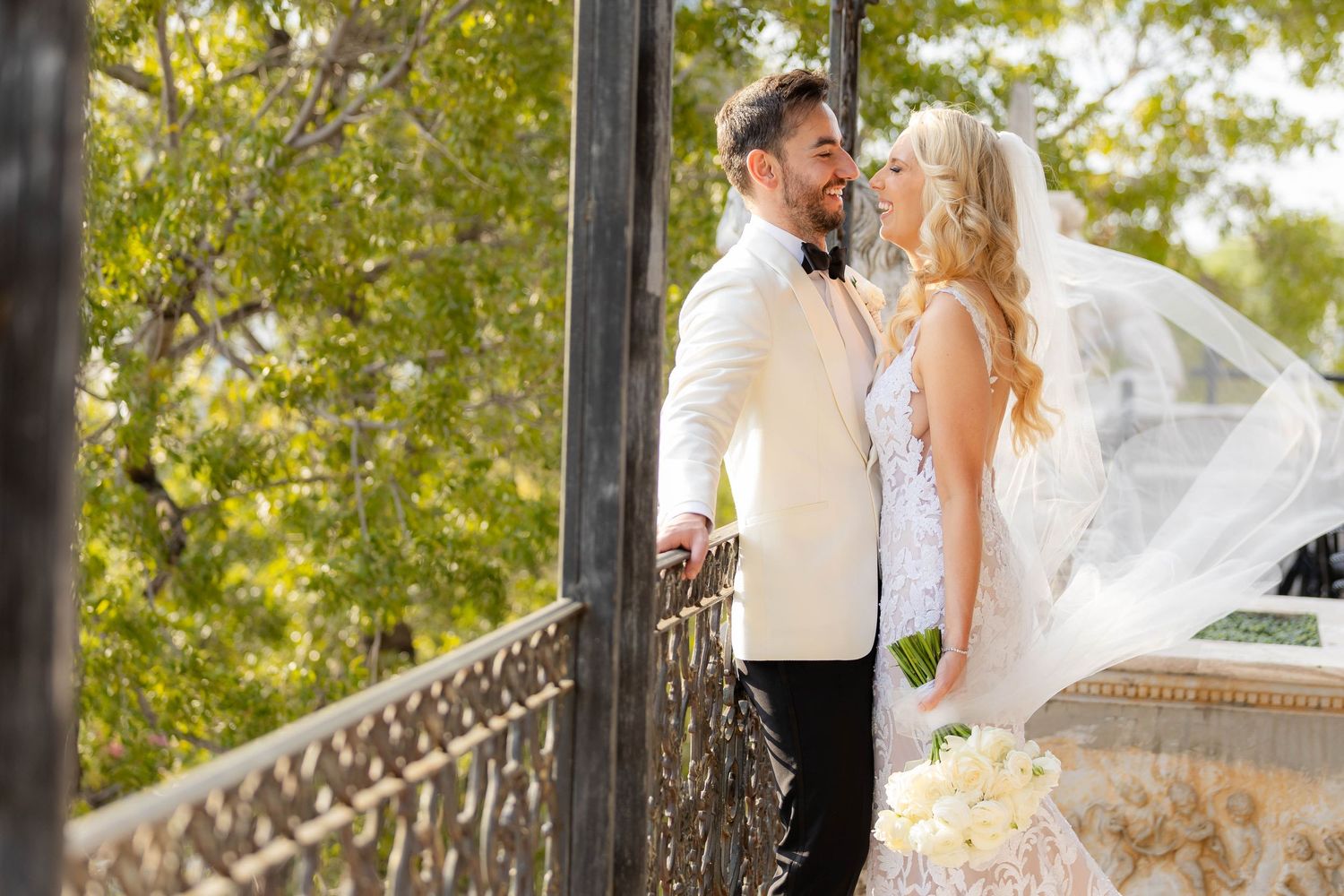 Romantic outdoor wedding photoshoot with venue pillars and greenery in the background.