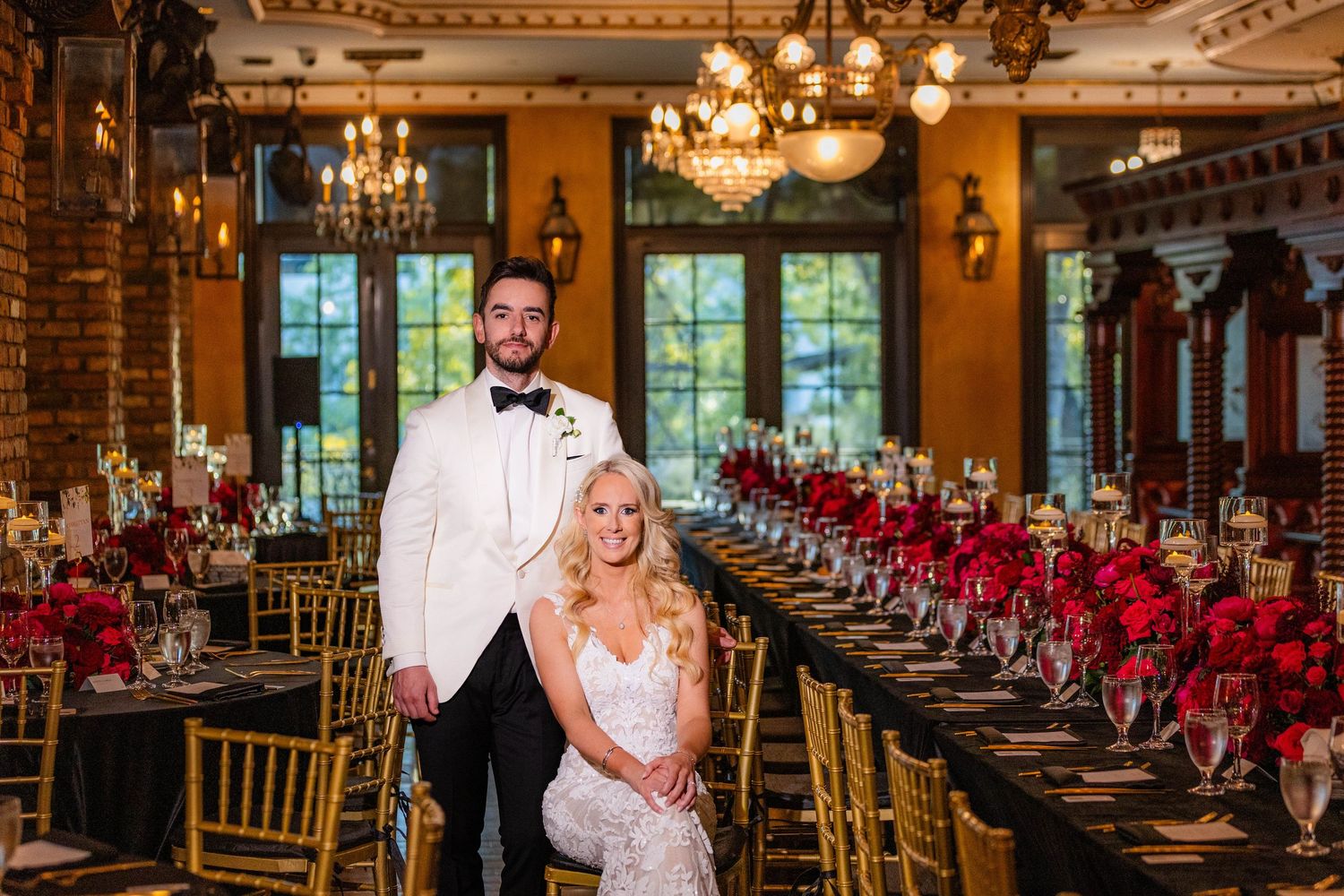 Elegant wedding reception hall with red and gold decor featuring chandeliers and chiavari chairs.