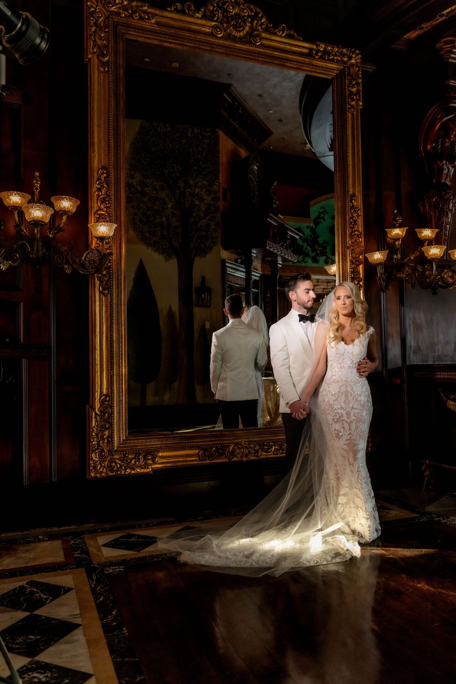Dramatic wedding portraits in a luxurious venue with ornate gold mirrors and romantic lighting.