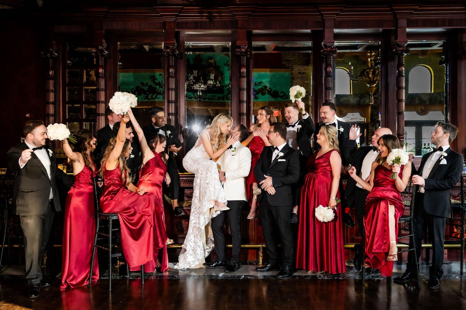 Bridal party performs during wedding reception against dark wood paneling with red and black color scheme.