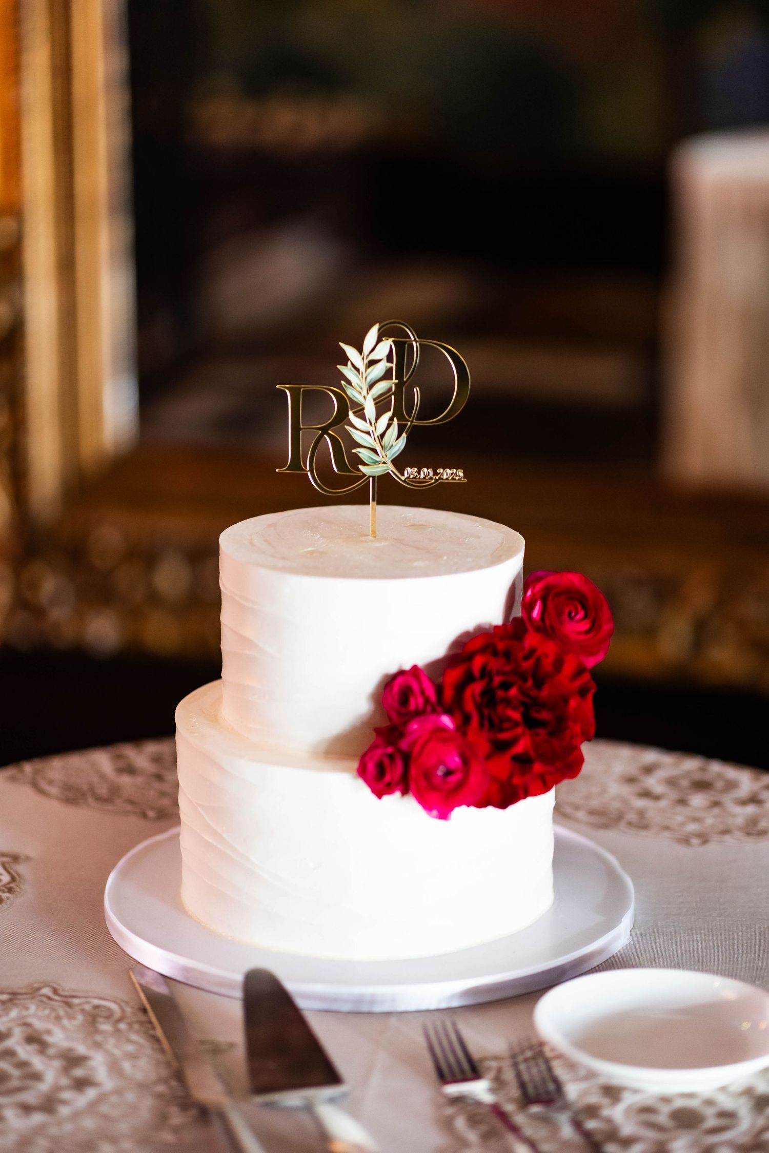 Elegant white wedding cake adorned with deep red roses sits on a delicate lace tablecloth.