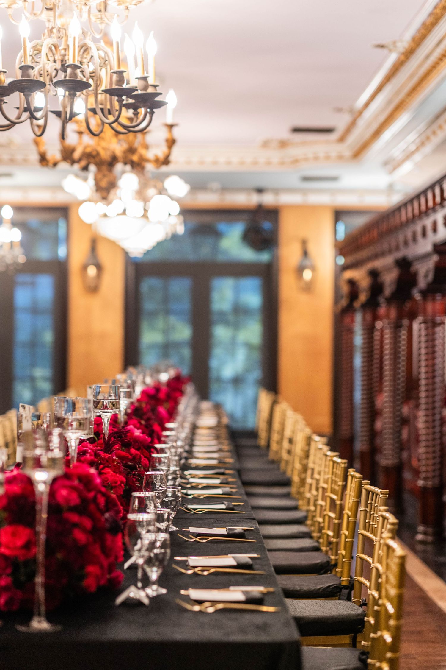 Elegant reception table setting with black linens, gold chairs, and deep red floral centerpieces.