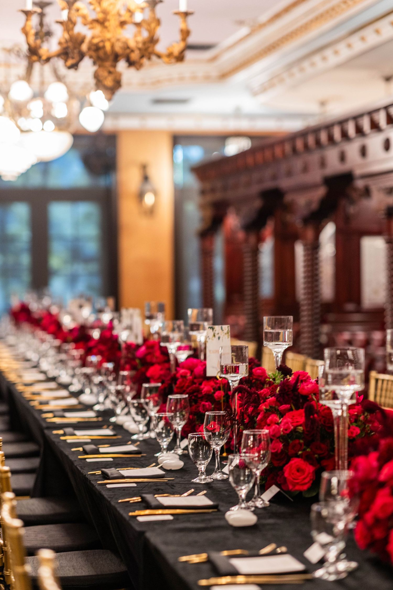 Elegant wedding reception table set with black linens and deep red rose centerpieces.