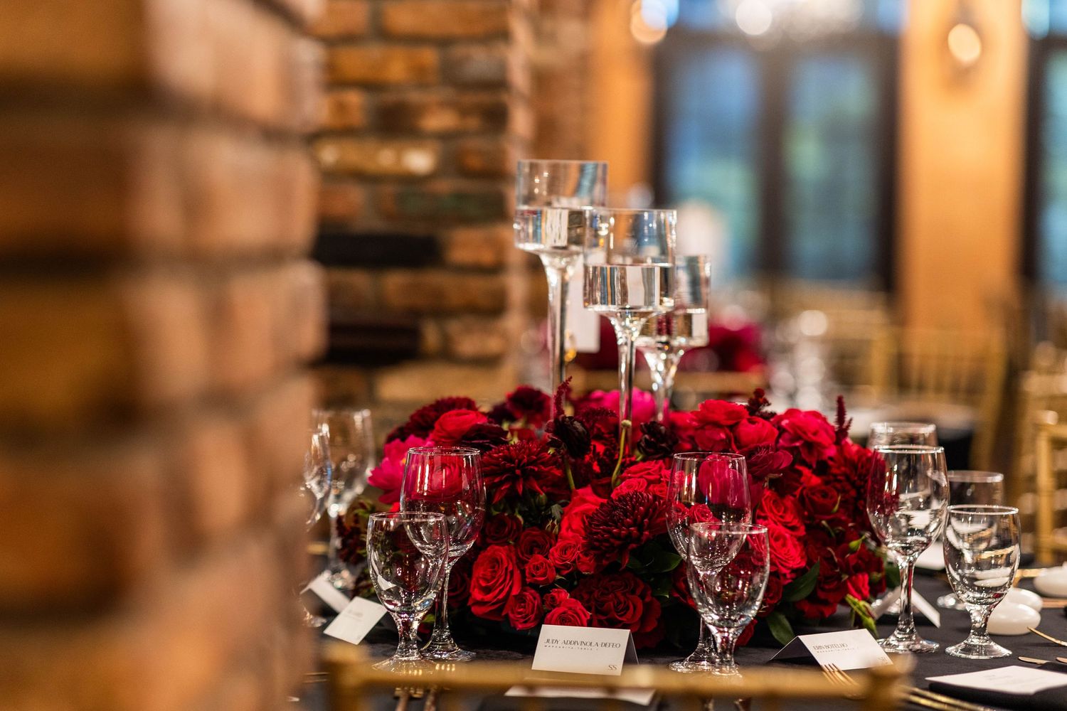Elegant wedding reception tables decorated with red rose centerpieces and wine glasses in rustic venue.