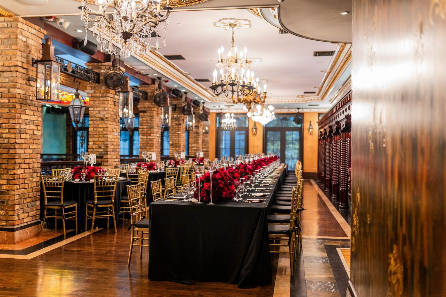 Elegant event venue with exposed brick walls, crystal chandeliers, and wood paneled walls in warm ambient lighting.