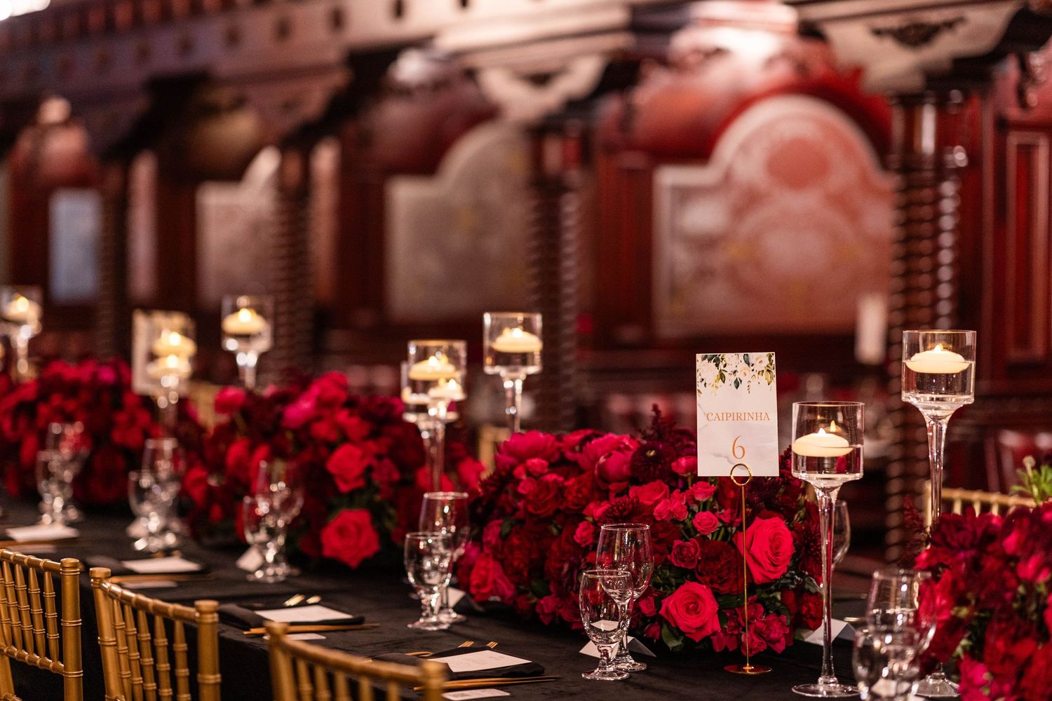 Elegant table settings with crystal glasses and deep red floral centerpieces in an upscale dining venue.