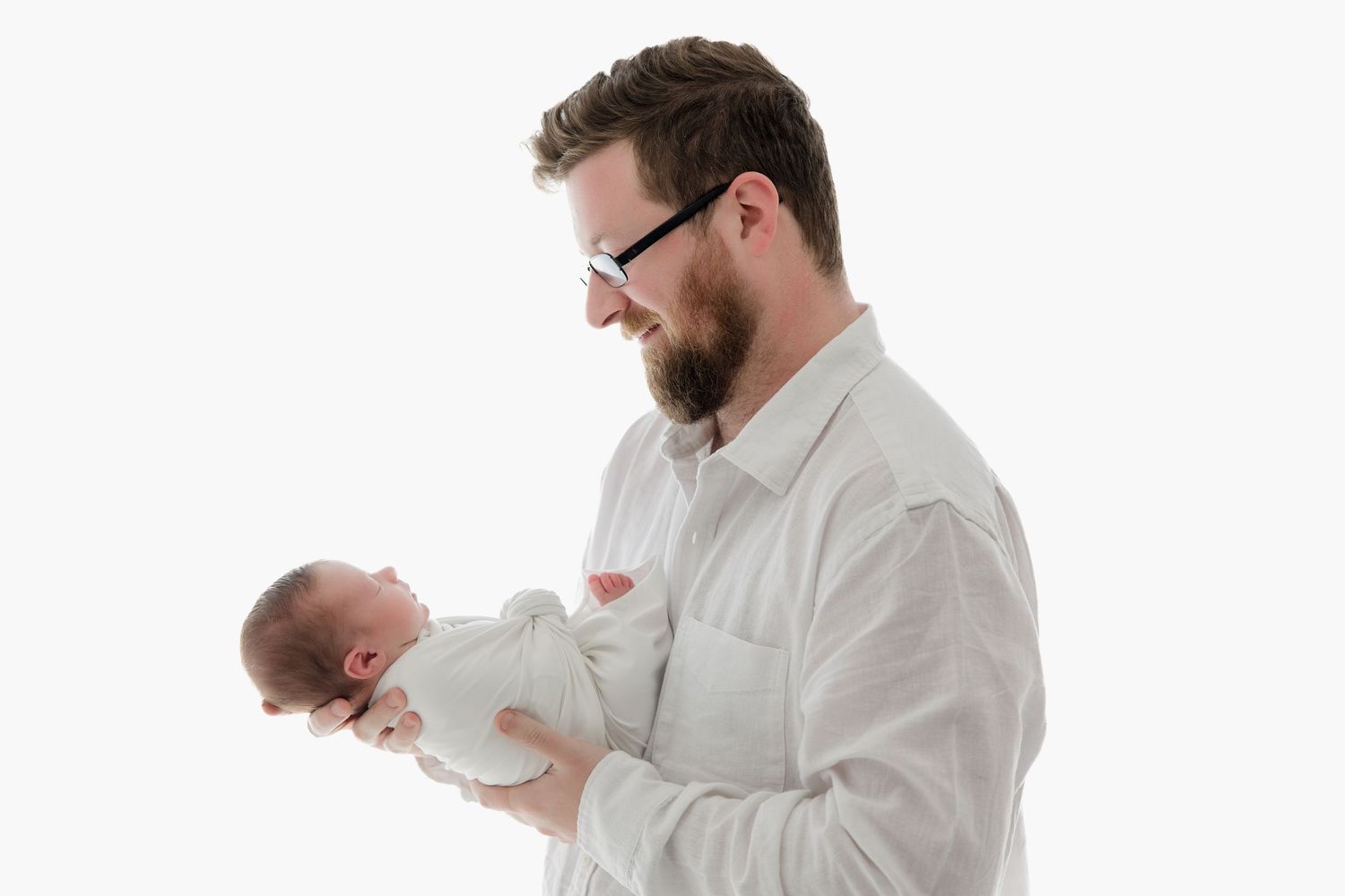 A person in a white button-down shirt gently holds and gazes at a swaddled newborn baby.