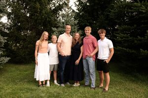 A group poses together on a grassy hill with evergreen trees in the background.