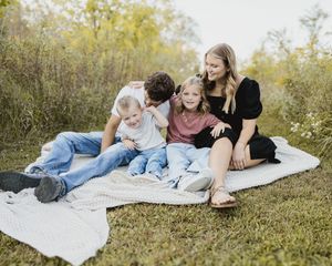 Family relaxing together on a white blanket in a grassy field at sunset.