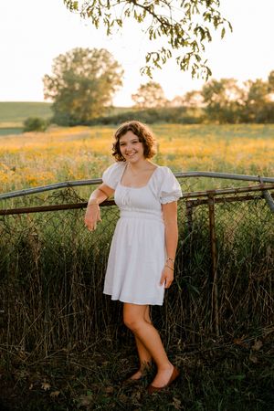 Person in white dress poses against rustic fence during golden hour photoshoot.