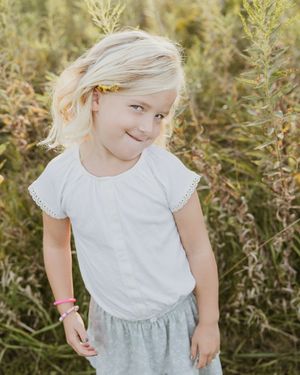 Young person in white dress twirling and playing in a wildflower field at sunset.