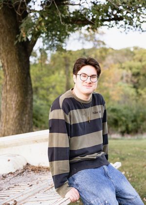 Person in glasses and striped sweater sitting casually on wooden steps in an outdoor autumn setting.