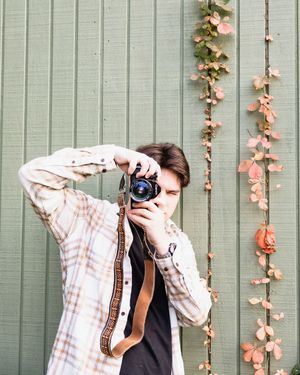 Photographer taking pictures with a DSLR camera against a green wall decorated with climbing pink flowers.