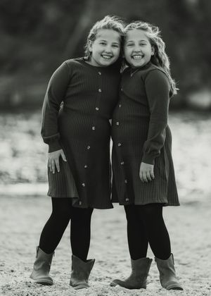 Two children in matching dark sweaters and pants stand together outdoors in a black and white vintage photograph.
