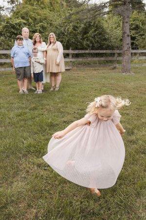 A child in a flowing dress twirls joyfully in a grassy field.
