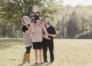 A group of four people standing together outdoors on a sunny day in a grassy field with trees in the background.
