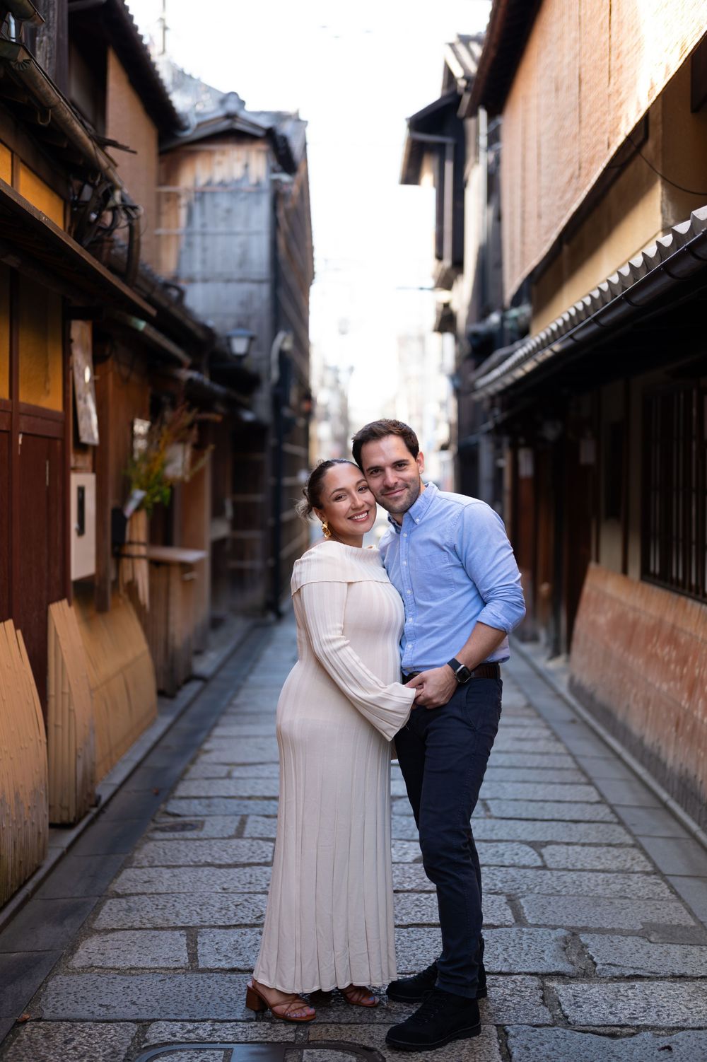Happy pregnant couple embraces in a narrow historic Japanese alleyway lined with wooden buildings.
