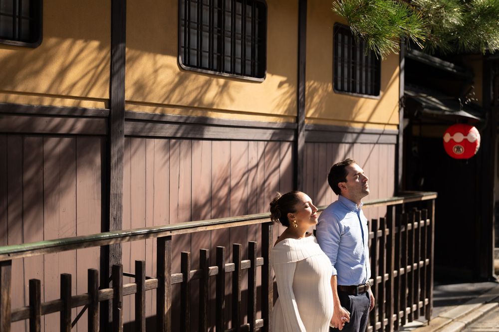 Couple looking up together outside a traditional Japanese wooden building with a red lantern.