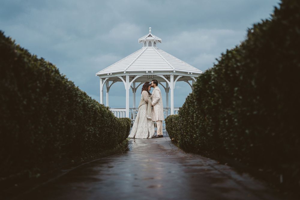 White wedding gazebo with decorated chairs creating an aisle between manicured hedges.