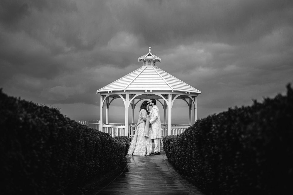 Dramatic black and white wide shot of a hilltop wedding gazebo under stormy skies.