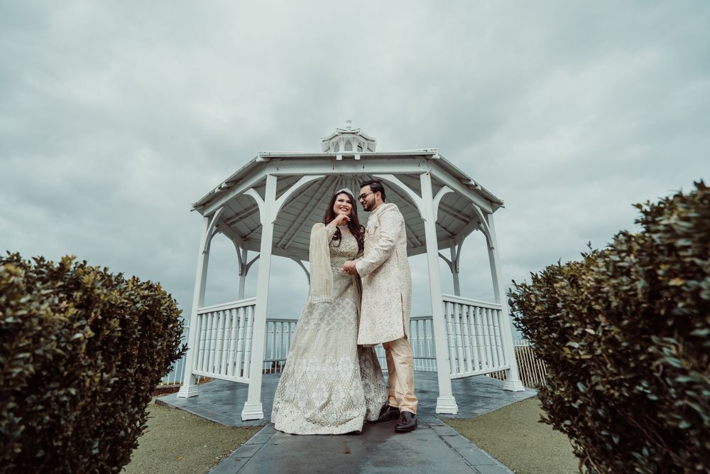 A couple poses under an elegant white gazebo on their wedding day with dramatic cloudy skies in the background.