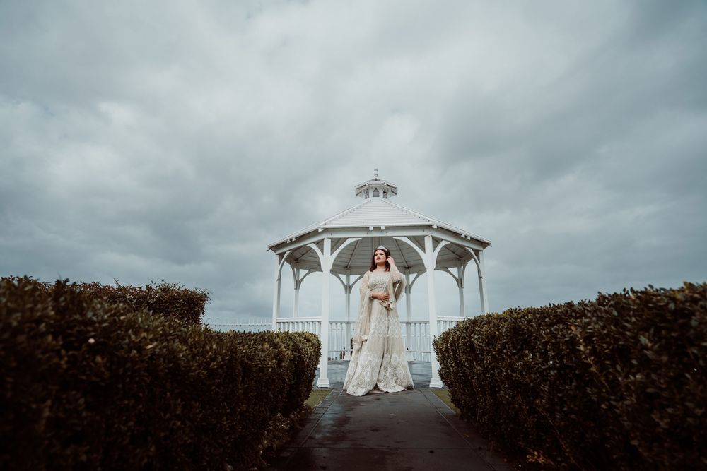 A white wedding gazebo stands at the end of a path lined with manicured hedges under overcast skies.
