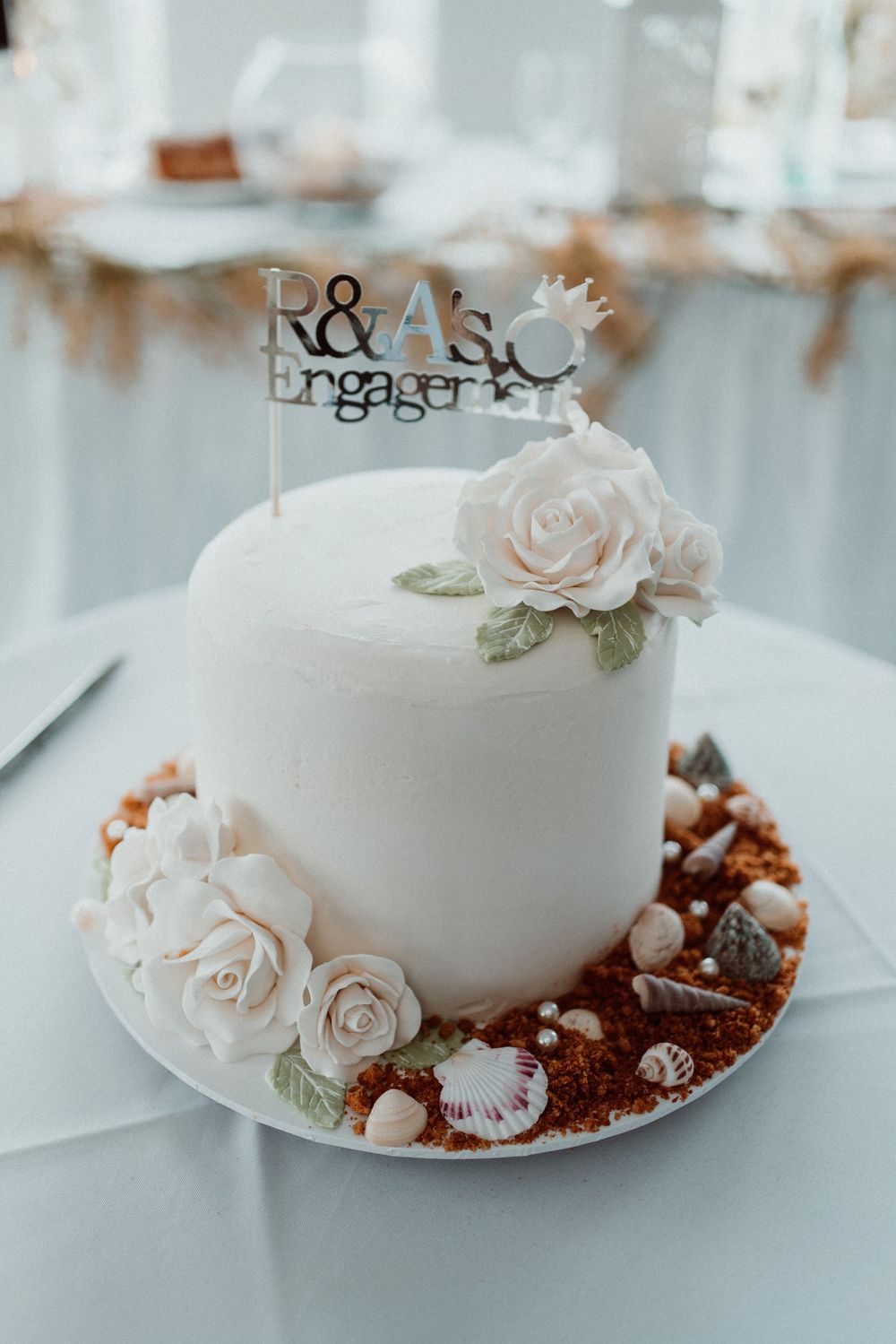 White wedding cake decorated with delicate blush roses and pearl accents sits elegantly on display.