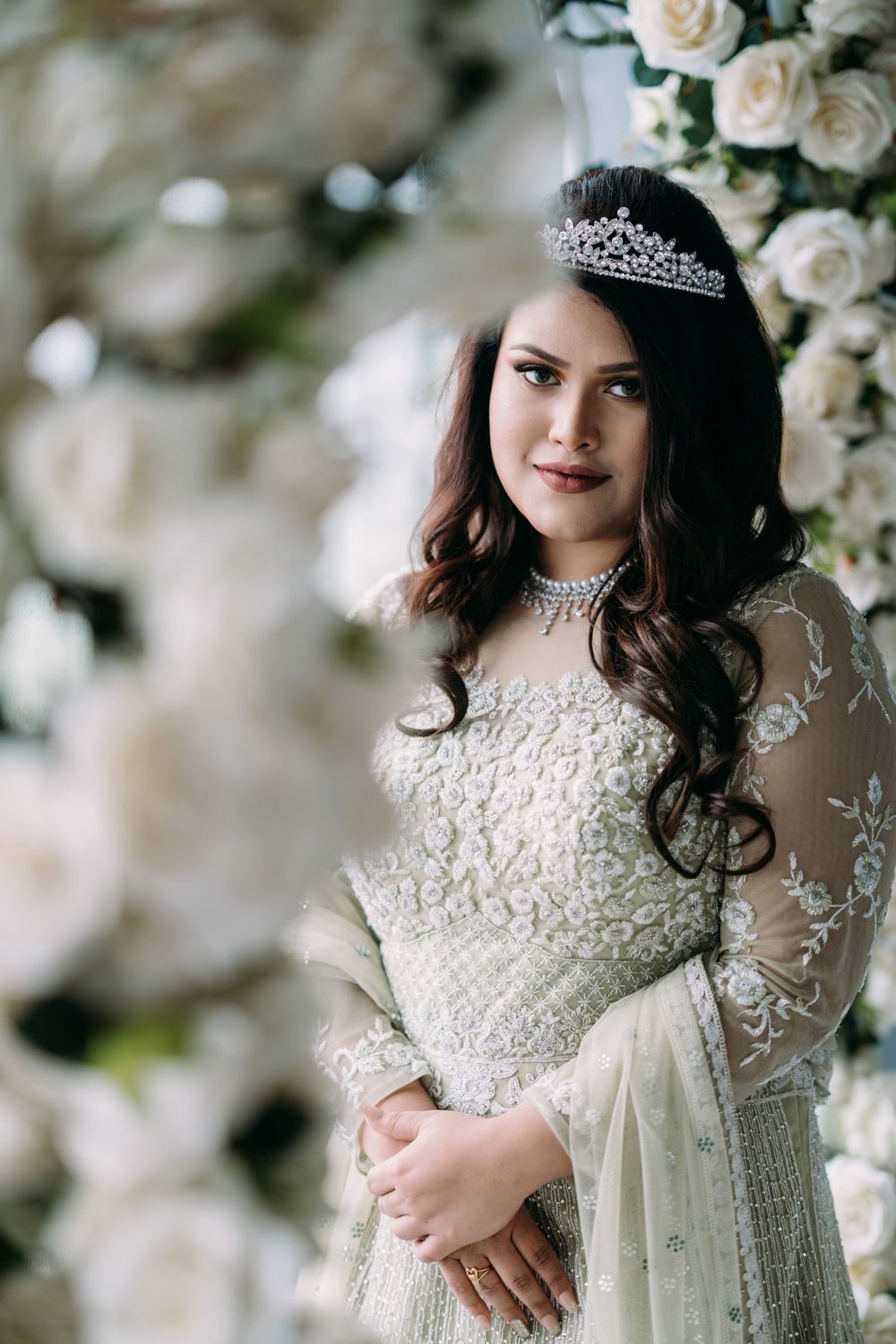 Elegant white lace wedding dress with intricate beading details and floral embellishments against a soft floral backdrop.
