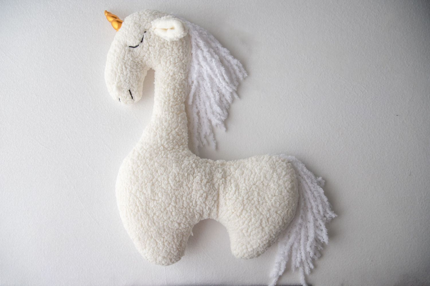 White fluffy unicorn stuffed animal toy with gold horn and yarn mane on white background.