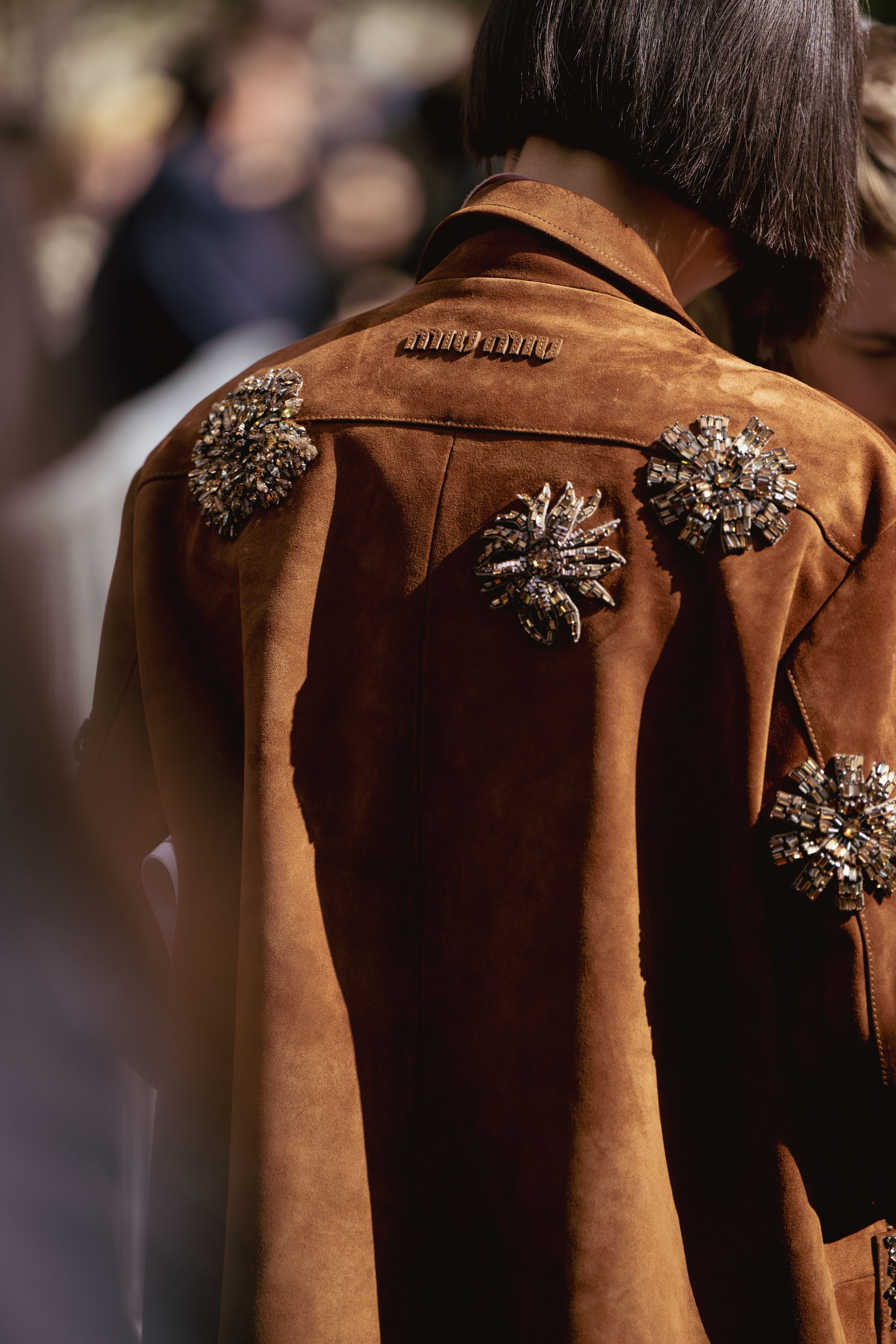 Close-up of brown suede jacket decorated with crystal embellishments shown from behind.