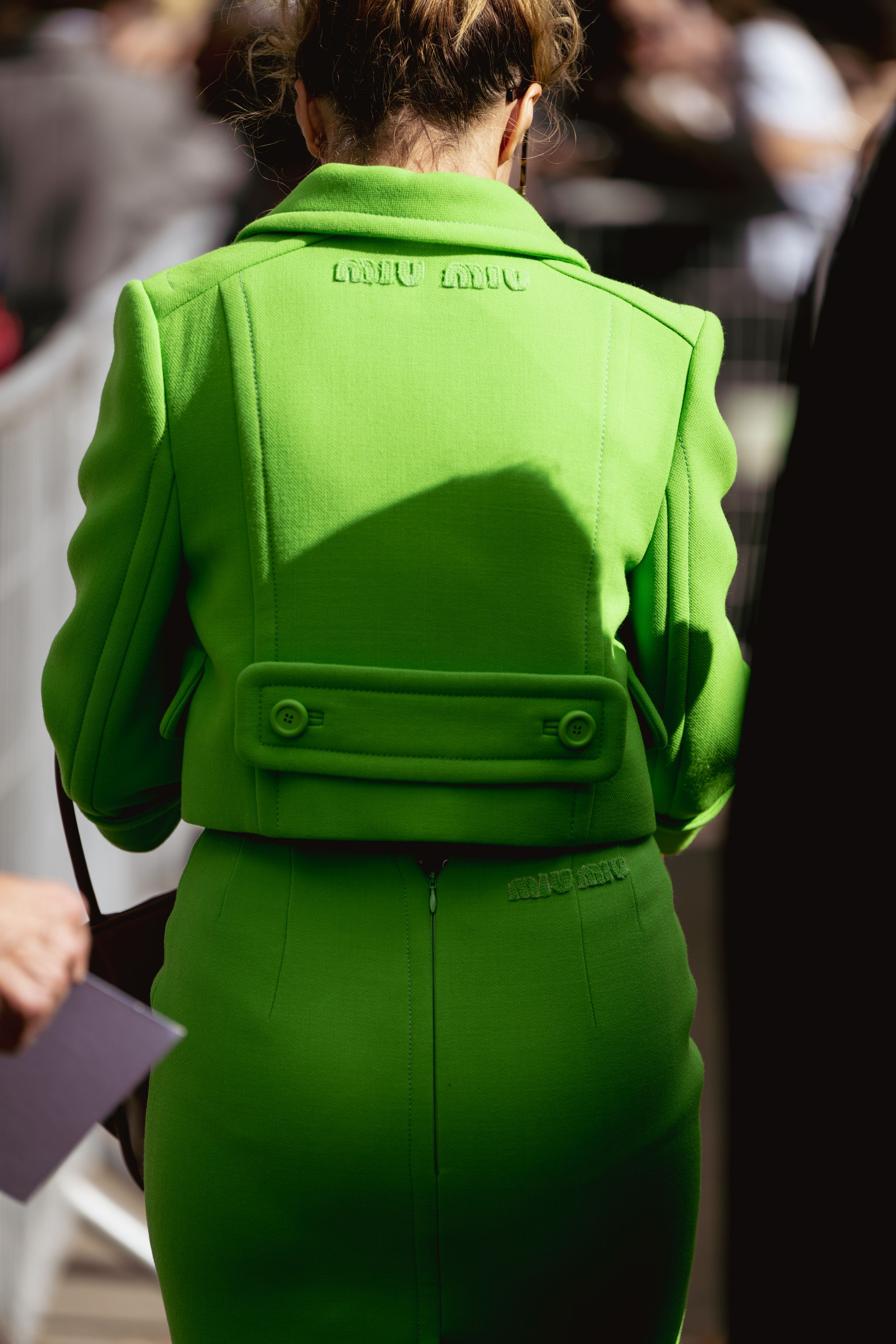 Back view of bright lime green fitted jacket with structural details and built-in bag.