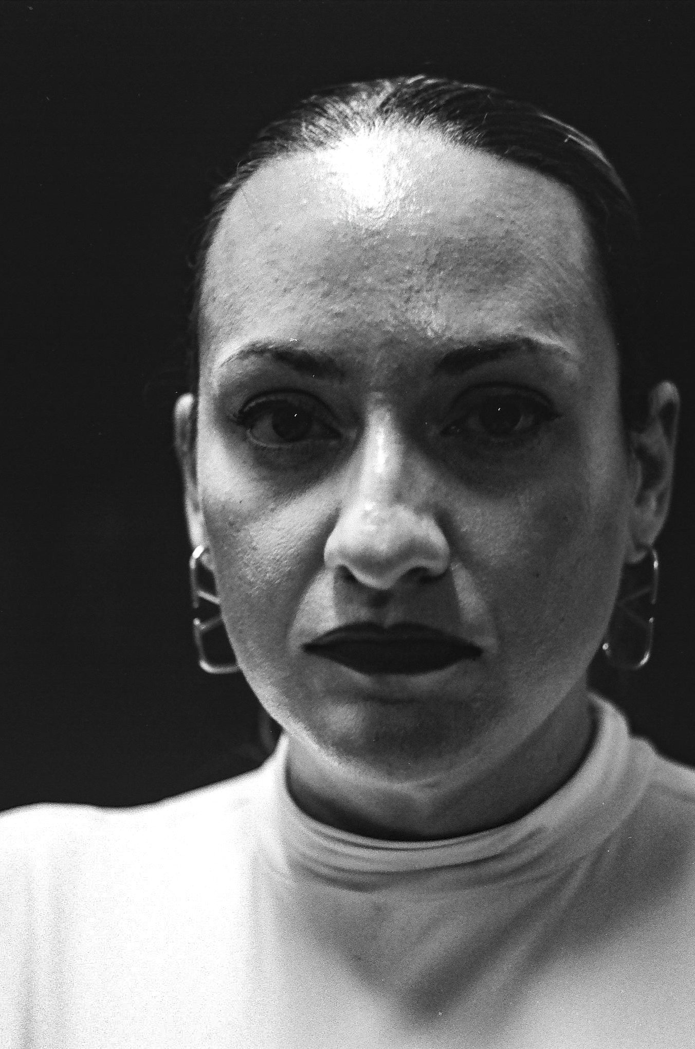 A dramatic black and white portrait with stark lighting and hoop earrings.