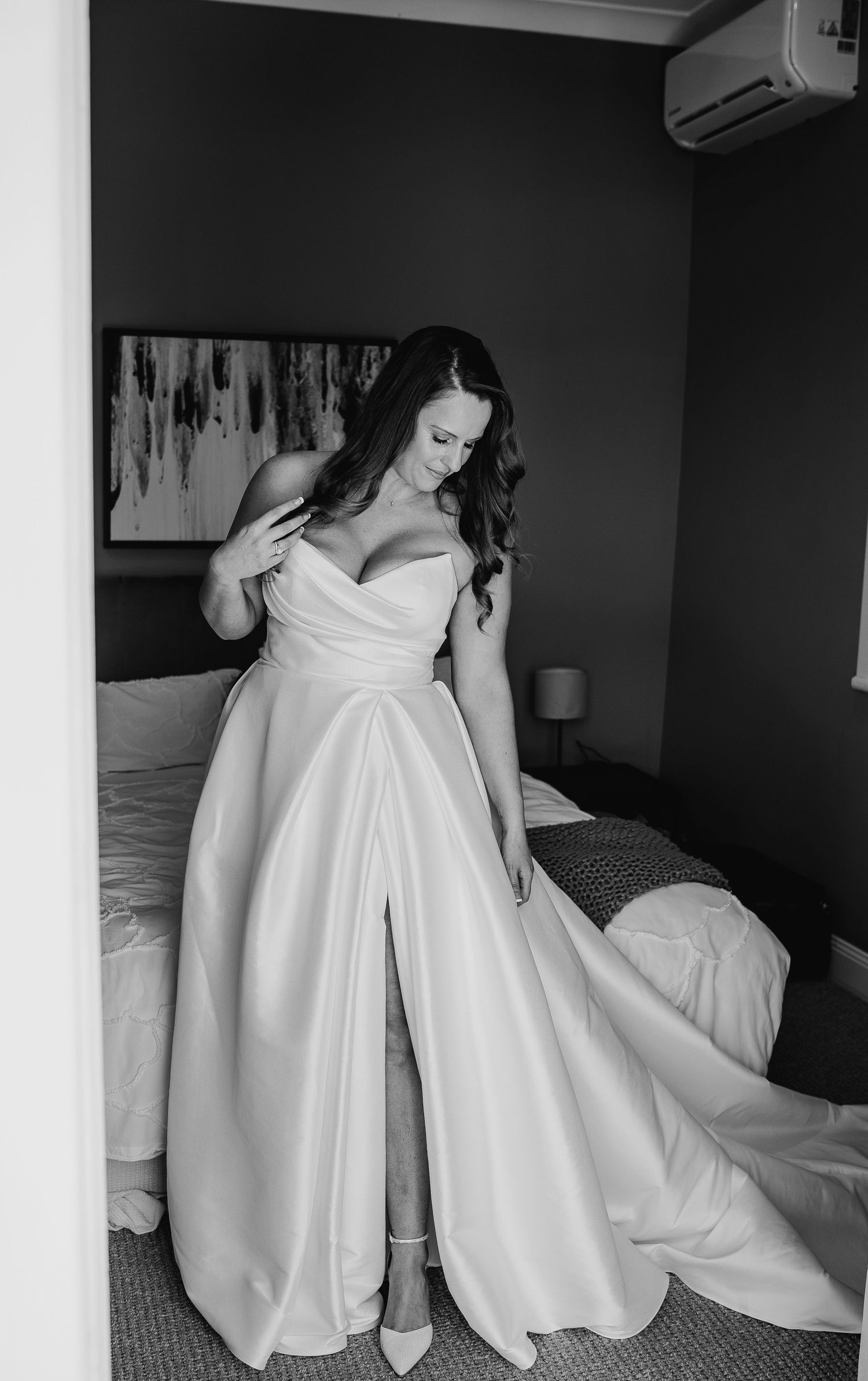Black and white photo of someone wearing an elegant strapless wedding gown with a side slit and flowing train.