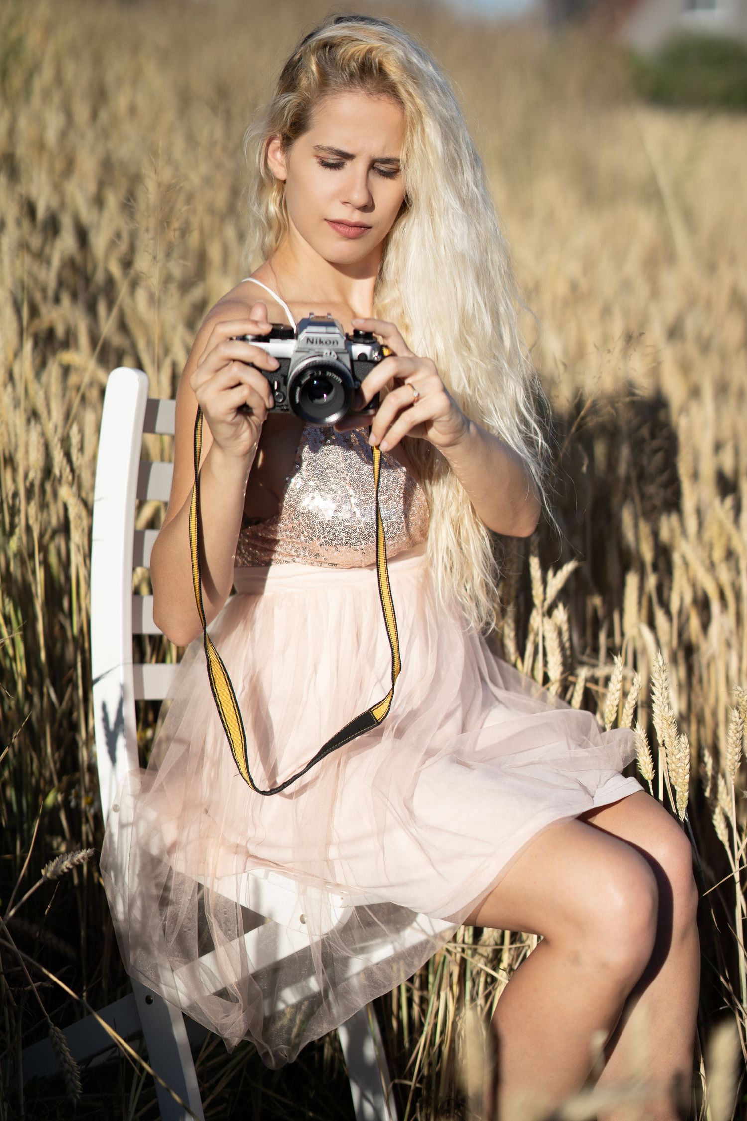 Beauty Portrait of a woman in light dress sitting in wheat field holding vintage camera.