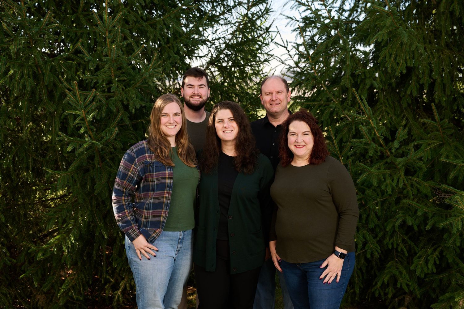 Group photo outdoors with evergreen trees in the background wearing casual fall clothing.