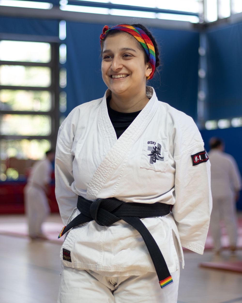 Martial artist in white gi and black belt wearing rainbow headband in training facility.
