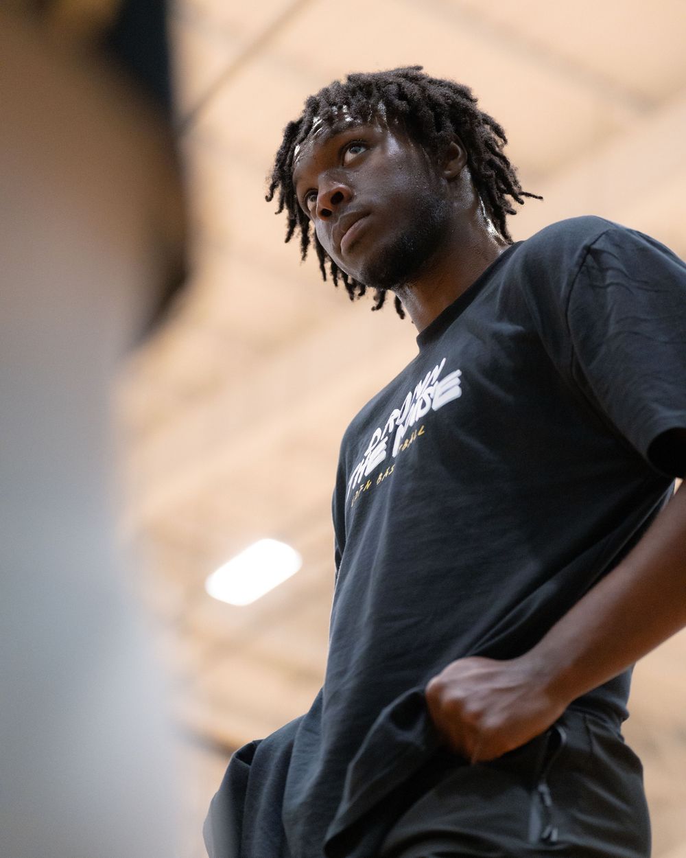 Basketball player in black t-shirt looks up during indoor practice session.