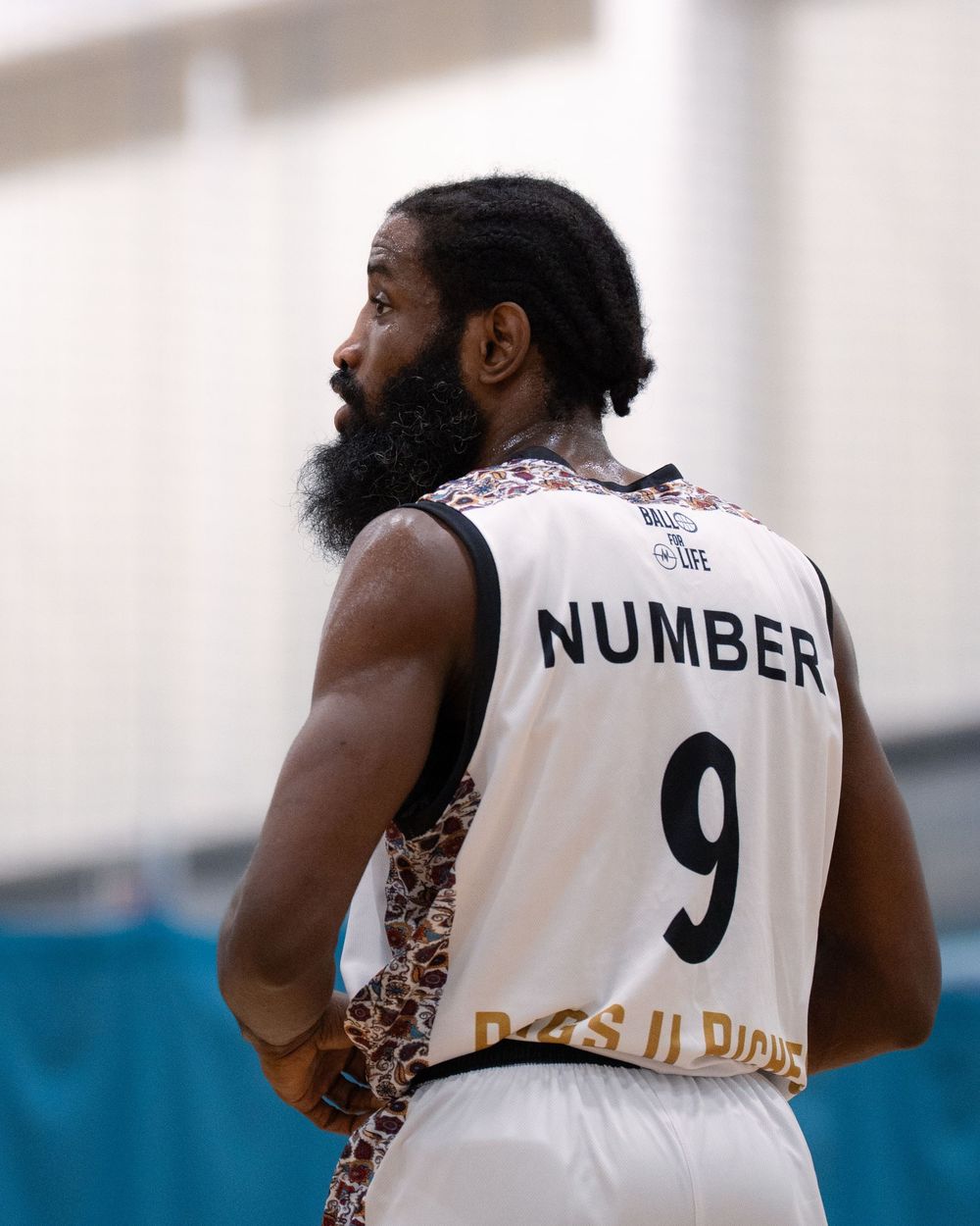 Basketball player wearing jersey number 9 stands with back turned to camera.