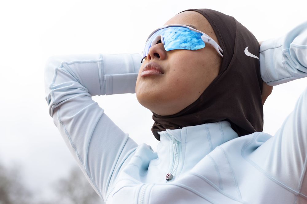 Athlete wearing a hijab and reflective sports sunglasses takes a break during outdoor exercise.