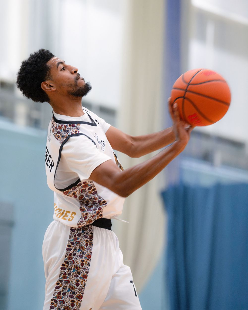 Basketball player in white jersey leaping high to slam dunk during an indoor game.