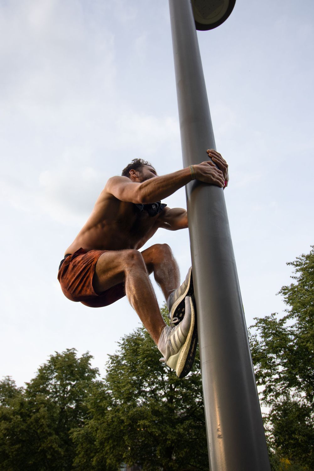 Athletic person climbing a metal pole outdoors against cloudy sky.